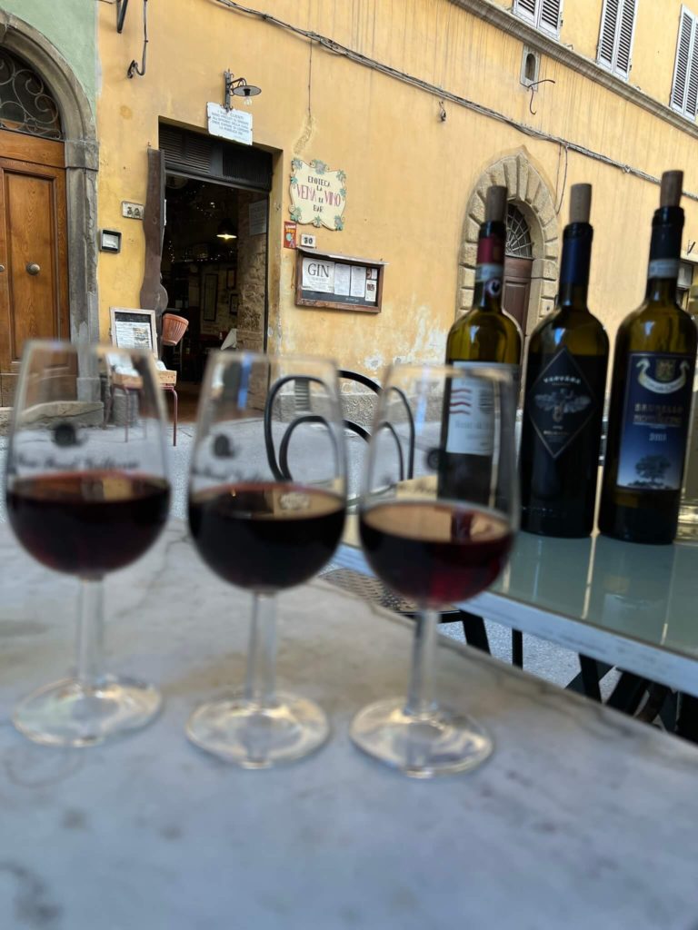 la vena di vino in the background with three unfocused glasses of red wine in the foreground